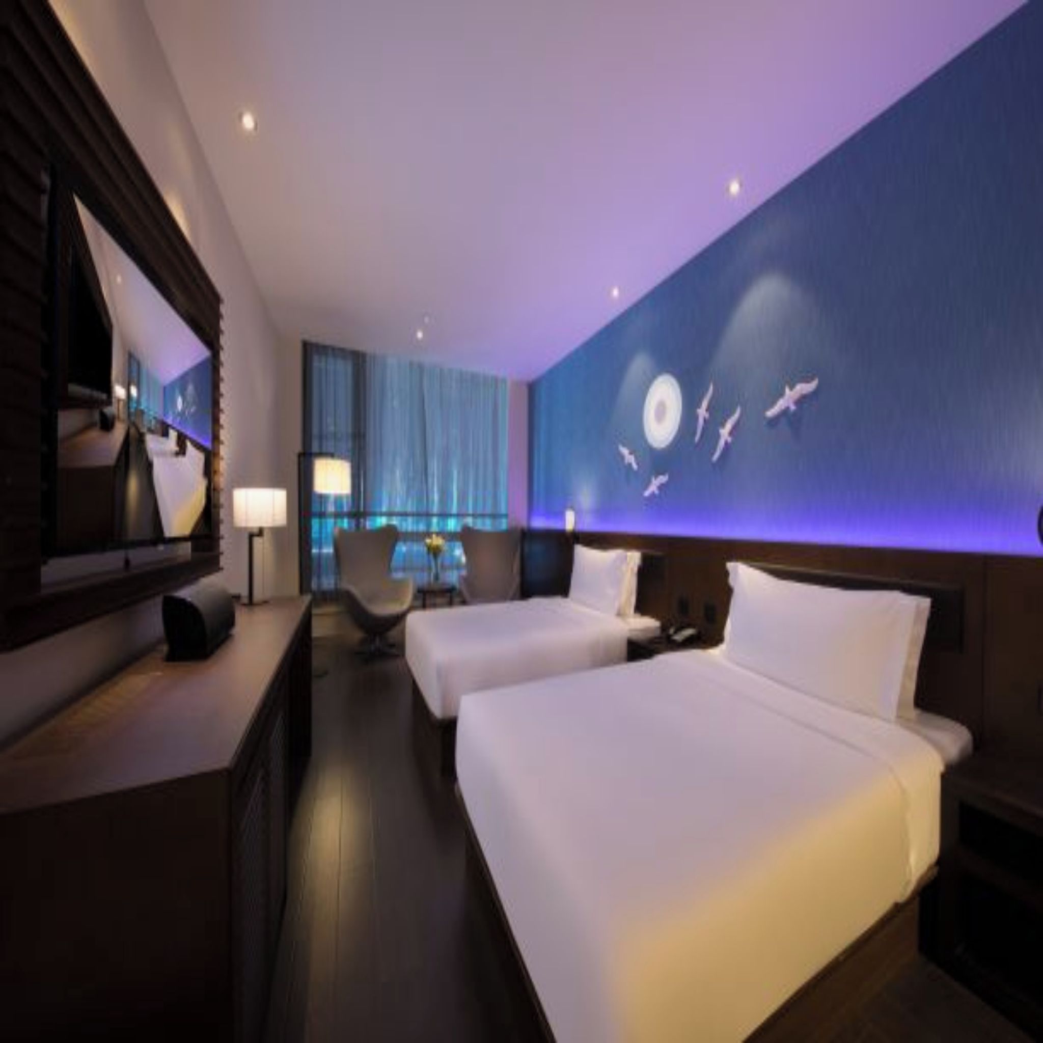 Habitación de hotel con dos camas, un escritorio, una silla y un mural grande en la pared.