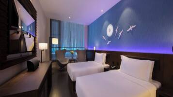 A hotel room with two beds, a desk, a chair, and a large wall mural.