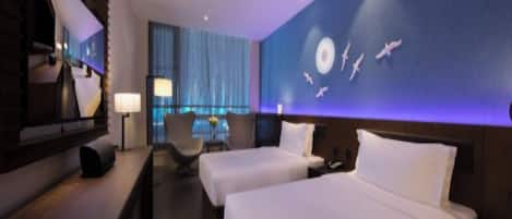 A hotel room with two beds, a desk, a chair, and a large wall mural.