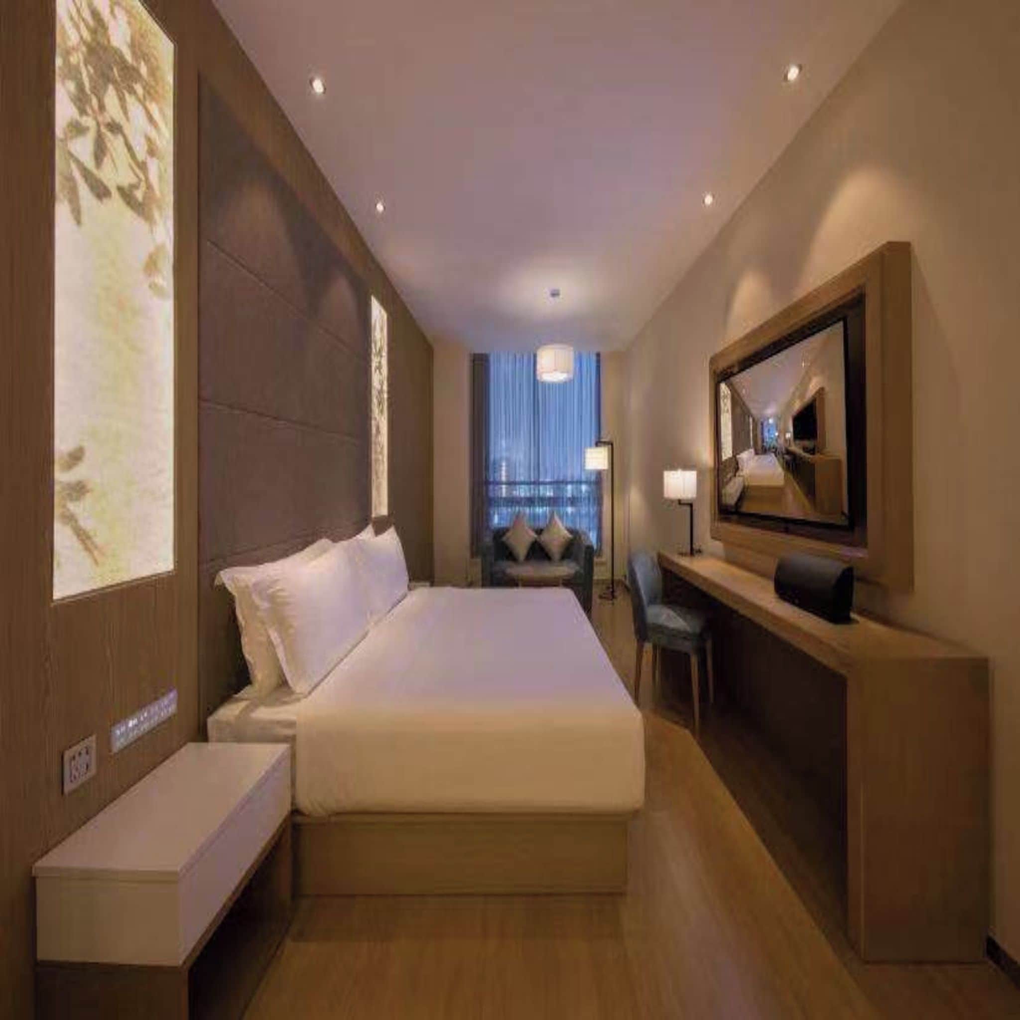 Une chambre d’hôtel avec un grand lit, un bureau, une chaise, une télévision et une grande fenêtre avec des rideaux.