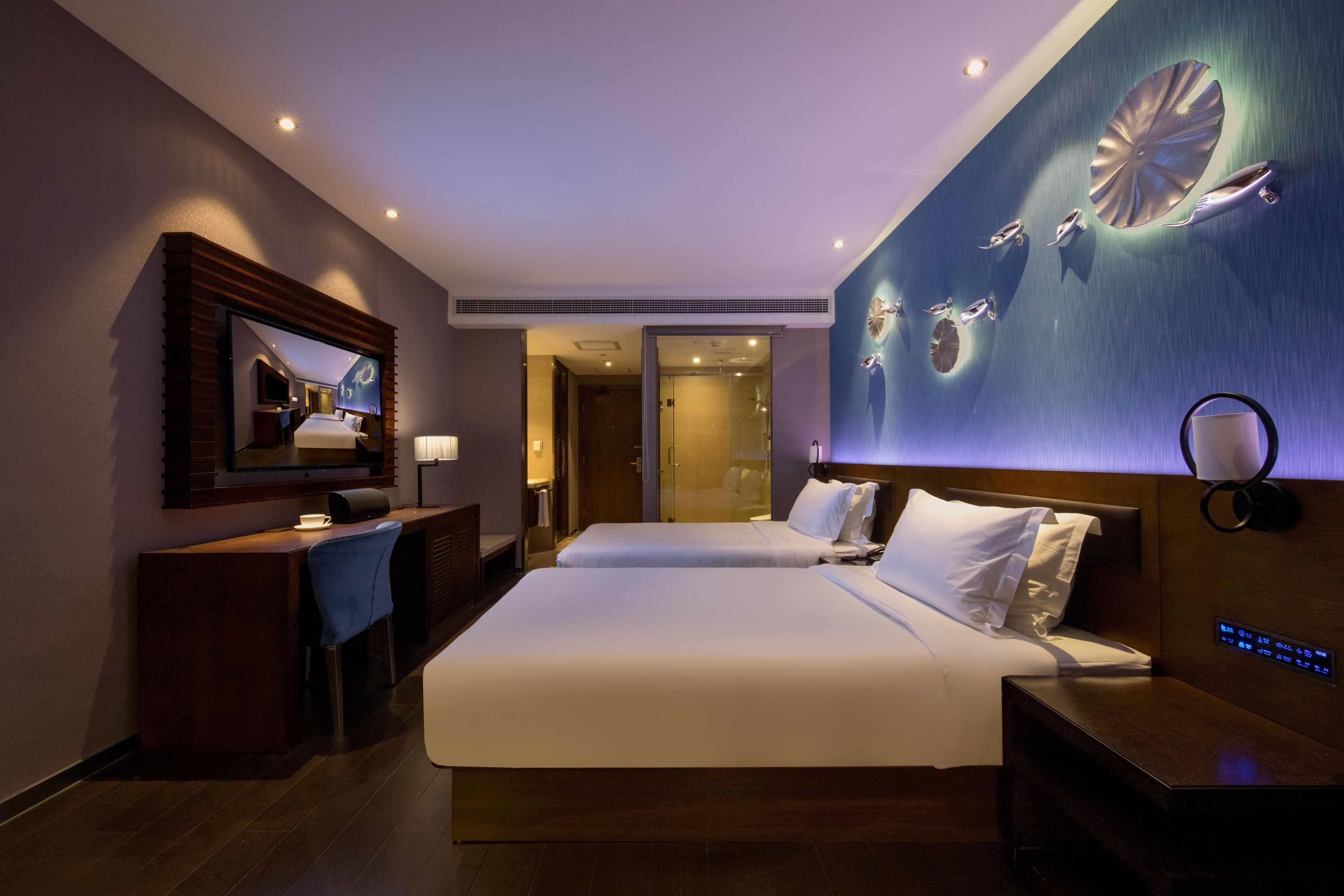 A hotel room with two beds, a desk, a TV, and a wall-mounted artwork.