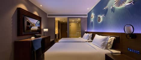 A hotel room with two beds, a desk, a TV, and a wall-mounted artwork.