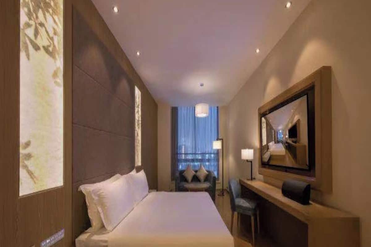 A hotel room with a large bed, a desk, a chair, a TV, and a large window with curtains.