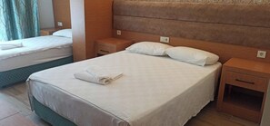 Uma cama de casal com uma toalha dobrada, um criado-mudo de madeira e uma mesa de cabeceira com abajur.