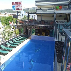 A pool area with lounge chairs, a sign for Britannia Hotel & Villas, and a view of the hotel buildings. - Britannia Apart & Villas Hotel (Kemer)