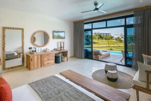 Una habitación de hotel moderna con un ventanal grande, un escritorio de madera, una cama y una zona de estar con vistas a una piscina y vegetación.