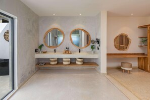 Un baño con dos espejos redondos, un tocador de madera y un taburete pequeño.