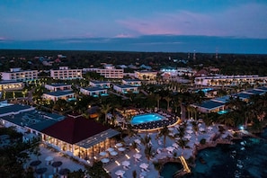 Vista aérea de un resort con varias edificaciones, una piscina y una zona de playa con sombrillas.
