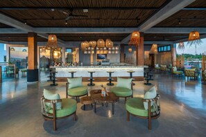 A spacious bar area with round tables and chairs, a long counter, and hanging wicker lamps.