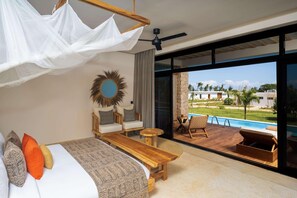 A bedroom with a bed, a wooden bench, a sofa, and a large window with a view of a pool and buildings.