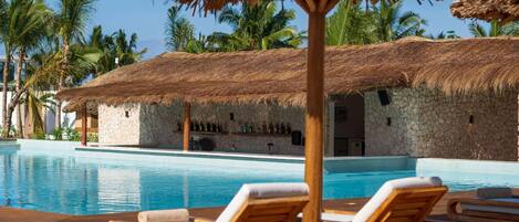 A poolside area with lounge chairs, a thatched-roof structure, and a stone building in the background.