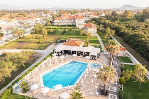 Un complex turístic amb una gran piscina, gandules i una zona coberta amb paraigües.