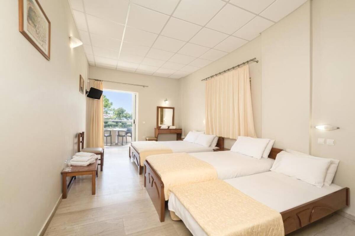 A hotel room with two beds, a desk with a chair, a small table, a mirror, and a view of the outdoors.