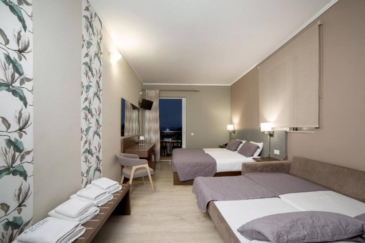 A hotel room with two beds, a desk, a chair, and a view of the city at night.