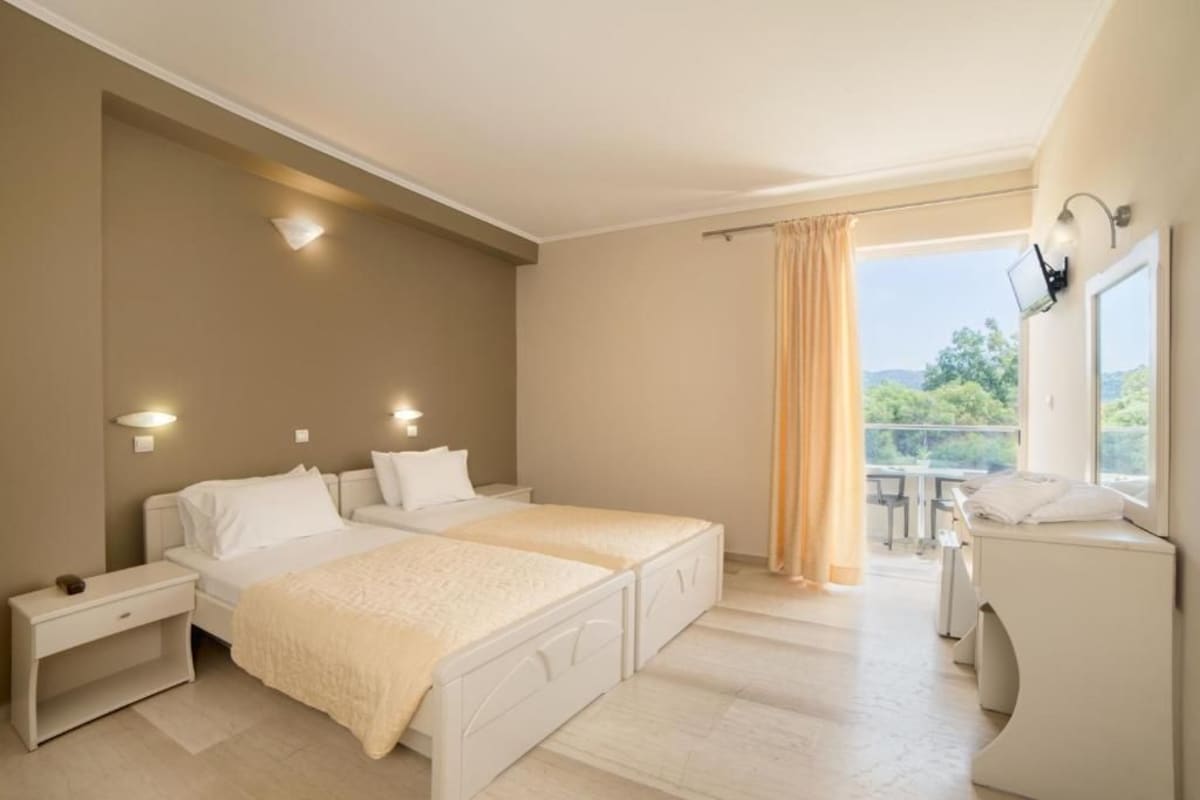 Ein Schlafzimmer mit einem großen Bett, Nachttischen, einem kleinen Schreibtisch, einem Fenster mit Vorhängen und einem Balkon.