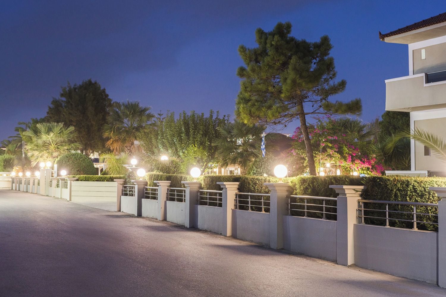 Un área residencial cerrada con una calle pavimentada, setos cuidados y un edificio moderno de techo plano.
