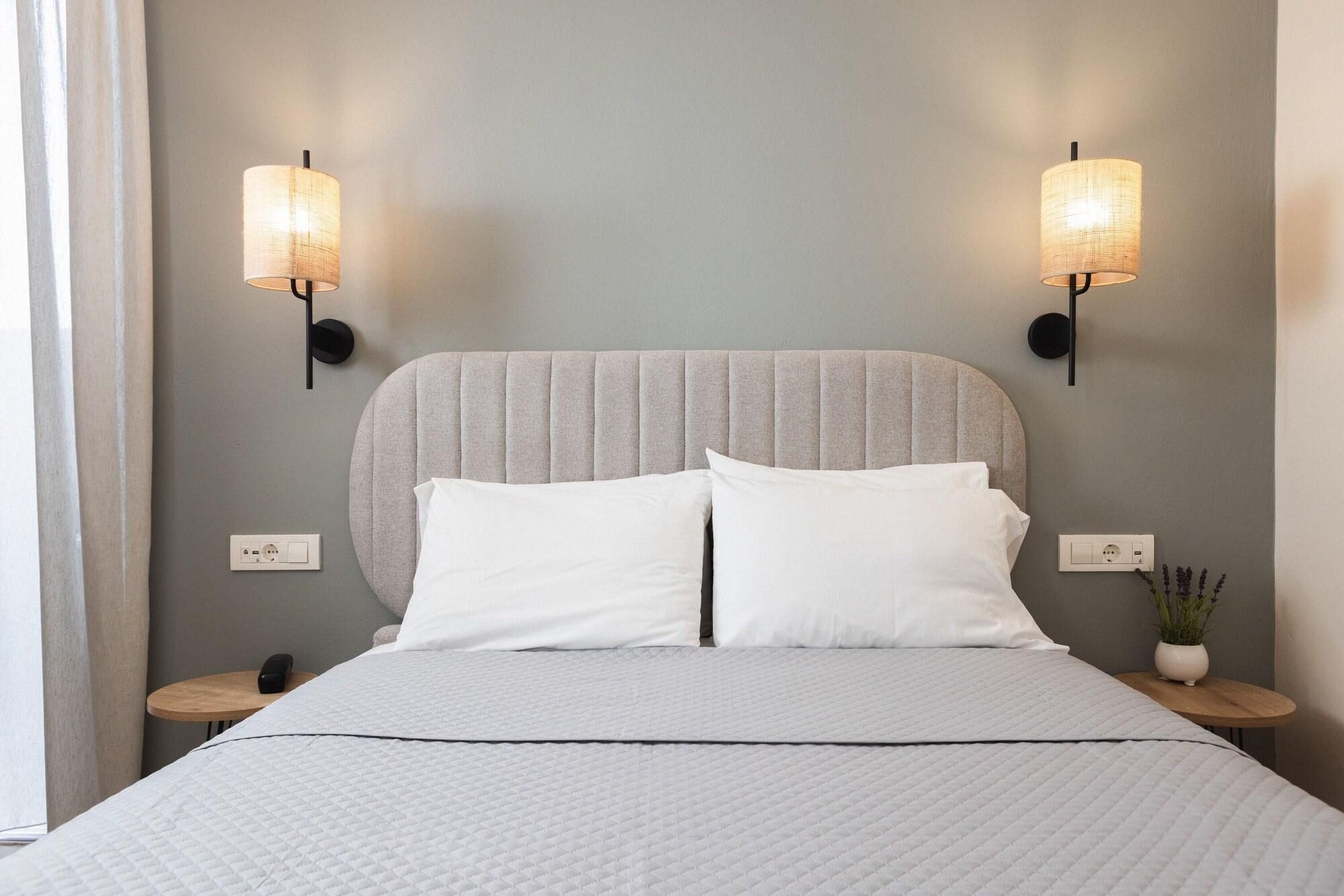 Een bed met een grijze hoofdbord, twee bedlampjes, een telefoon op het nachtkastje, en een kleine bloempot met plant.