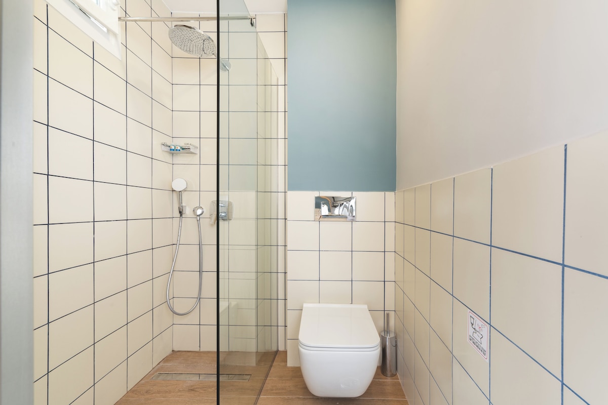 Ein Badezimmer mit weißen Fliesen, einer Duschkabine aus Glas, einer Toilette und einem Waschbecken.