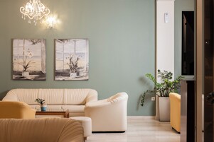 Un salón con un sofá beige, un sillón amarillo, una mesa de centro y dos cuadros en la pared.