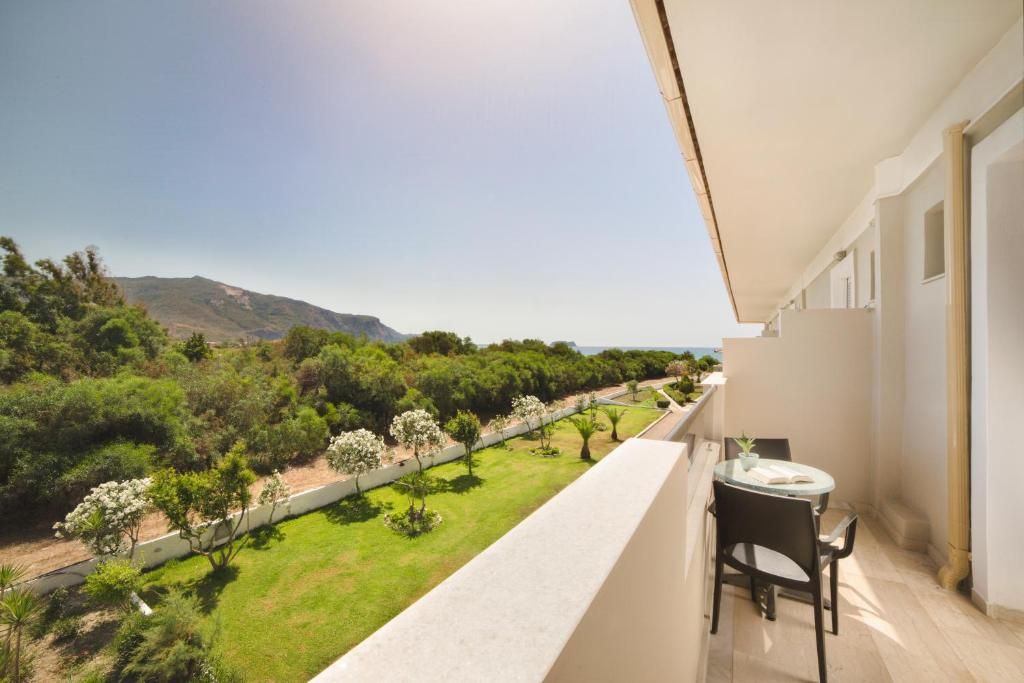 A balcony with a table and chairs, overlooking a landscaped garden and distant mountains.