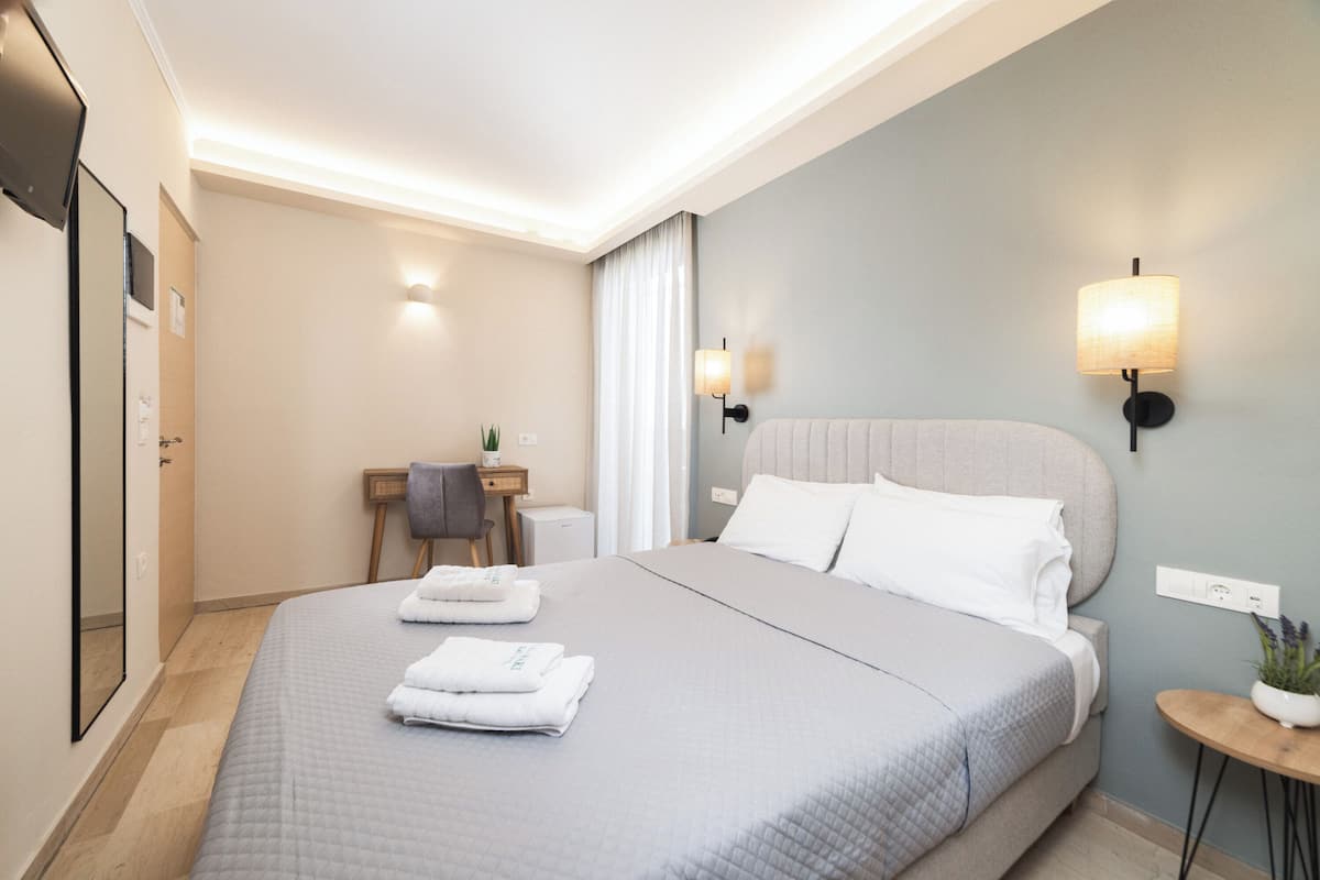 A modern hotel room with a large bed, bedside lamps, a desk with a chair, and a small table with a plant.