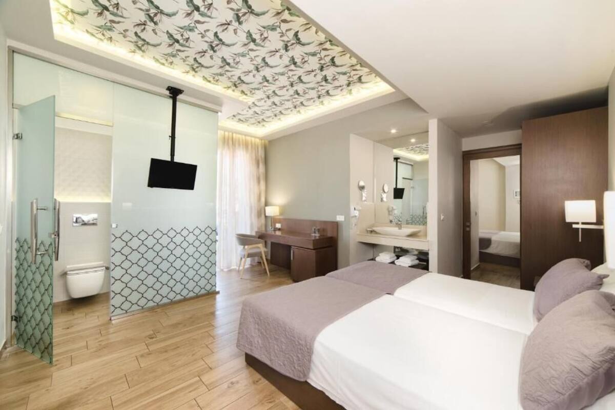 A hotel room with a bed, a desk, a mirror, a TV, and a bathroom.