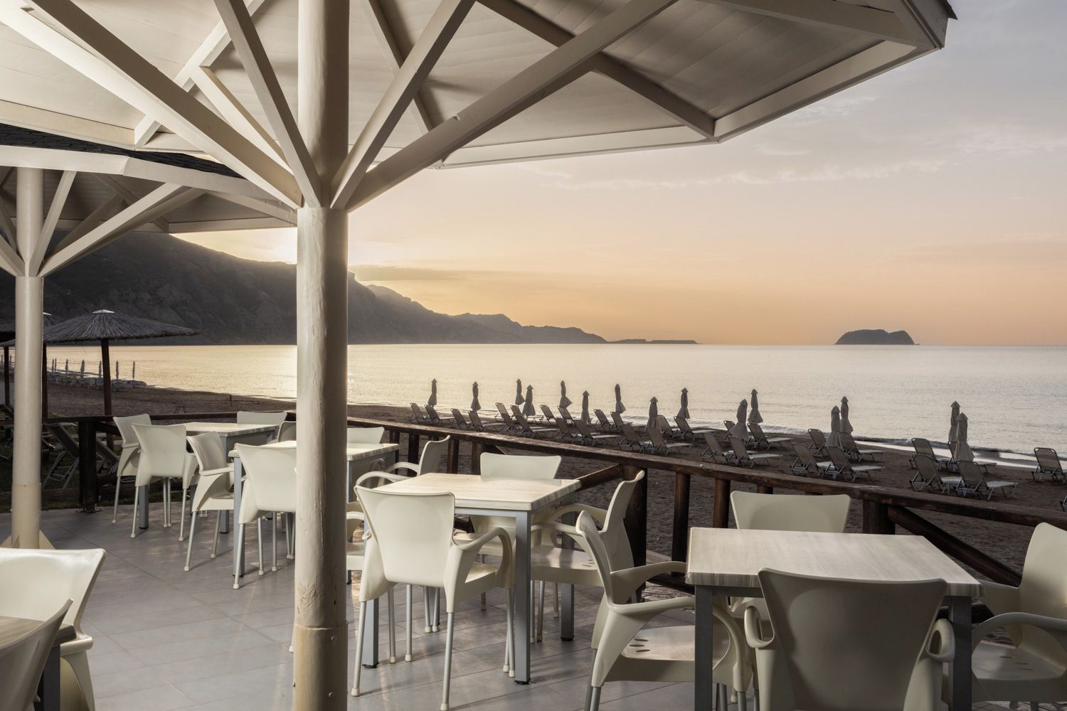 An outdoor seating area with tables and chairs, overlooking a body of water and distant mountains.