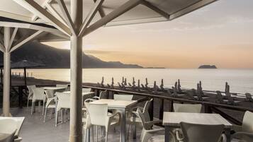 An outdoor seating area with tables and chairs, overlooking a body of water and distant mountains.