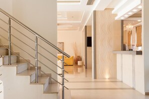 Een moderne hotel lobby met een trap, een receptiebalie en een golvend wandontwerp.