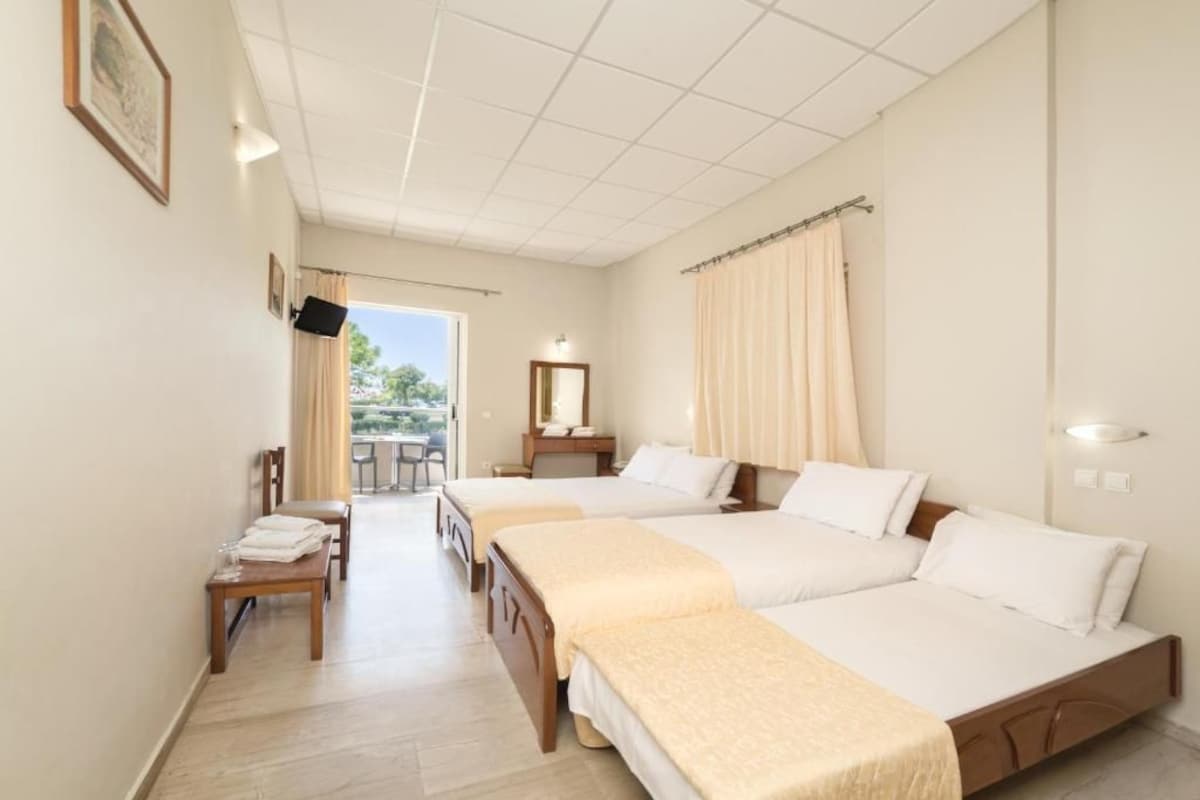Ein Hotelzimmer mit zwei Betten, einem Schreibtisch mit Stuhl, einem kleinen Tisch, einem Spiegel und Blick ins Freie.