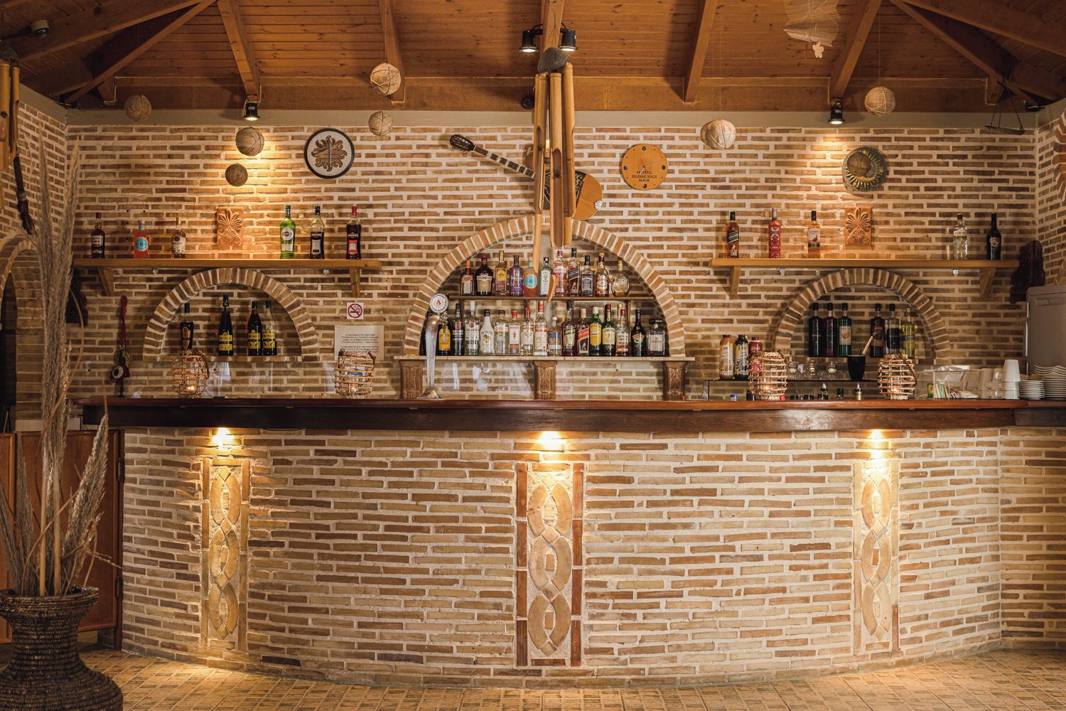Zona de bar con paredes de ladrillo, vigas de madera y estanterías llenas de botellas de licor.