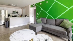 Una sala de estar moderna con un sofá gris, dos mesas de centro de mármol y una pared de acento verde.