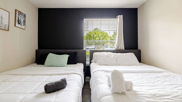 Habitación de hotel con dos camas, una ventana con persianas y vistas al exterior con vegetación.