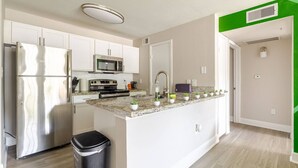 Una cocina moderna con electrodomésticos de acero inoxidable, una encimera de granito y un pequeño cubo de basura.
