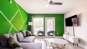 Una sala moderna con una pared verde de acento, un sofá gris, dos sillones, una mesa redonda y un televisor montado en la pared.