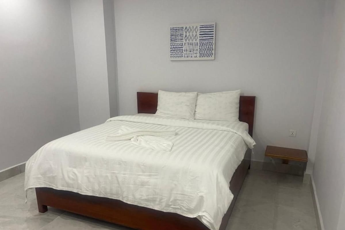 Un dormitorio con cama, mesita de noche, una obra de arte en la pared e interruptor de luz.