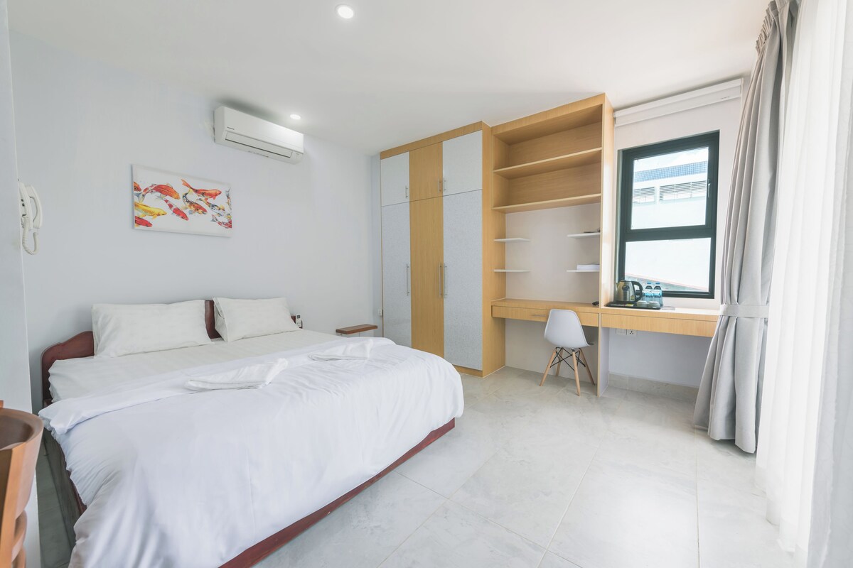 A bedroom with a bed, a desk, a chair, a wardrobe, and a window with curtains.