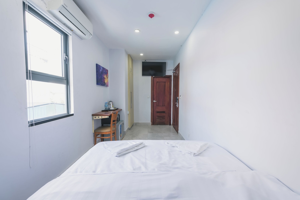 Habitación de hotel con cama, escritorio, silla, ventana y puerta.