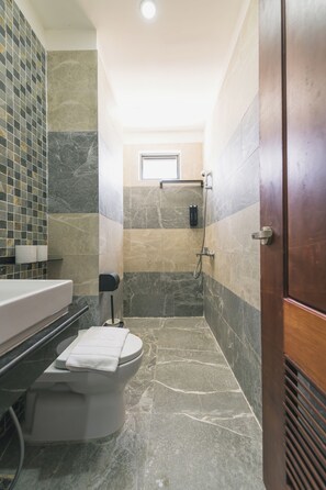 Un baño con inodoro, lavamanos y zona de ducha, con pared de azulejos y puerta de madera.