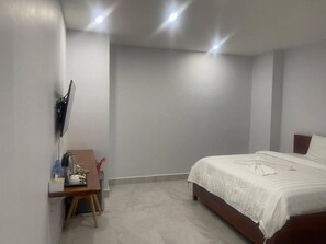 Un dormitorio con cama, un escritorio con silla, un televisor de pantalla plana montado en la pared y una lámpara en el techo.
