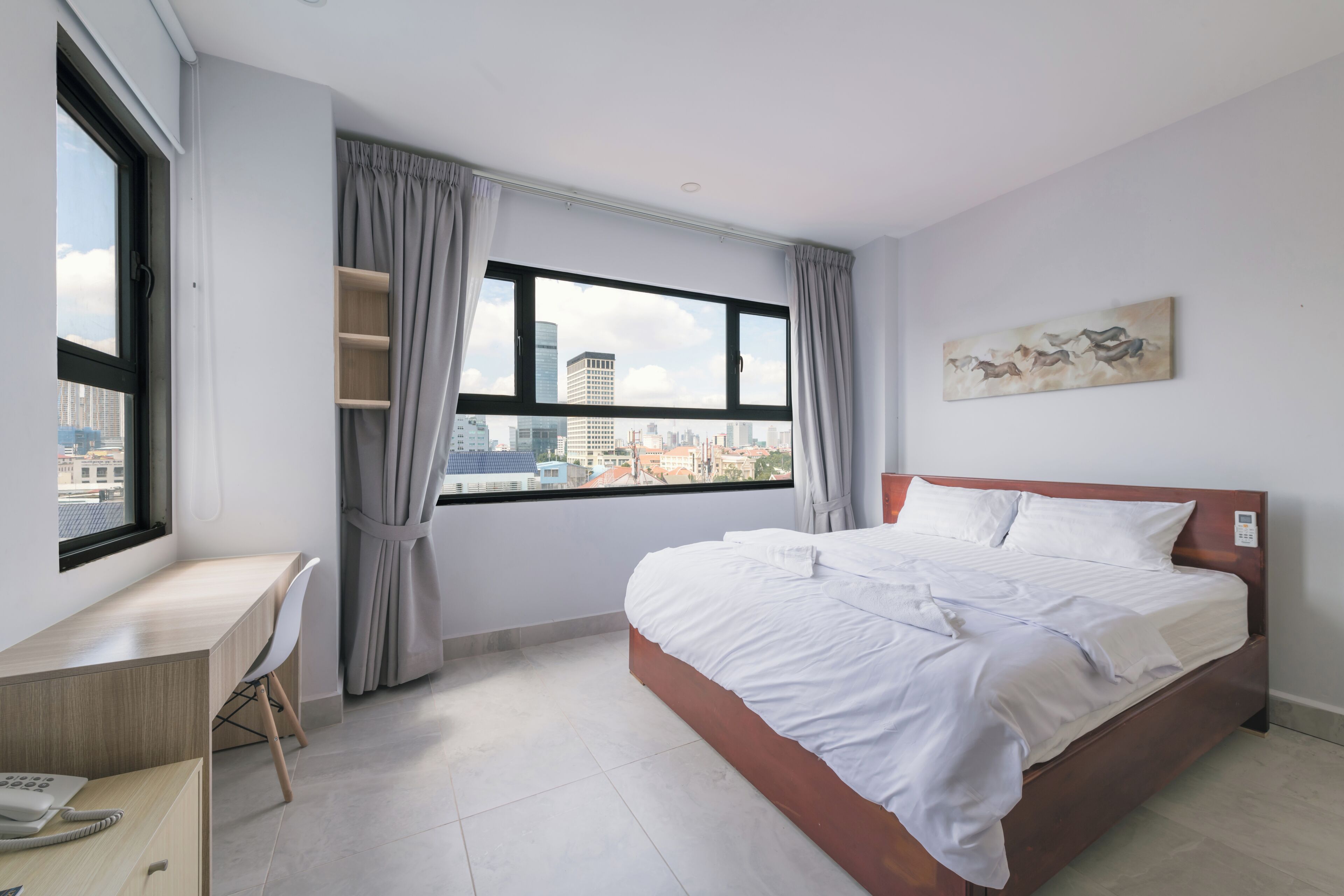 Moderni hotellihuone, jossa on suuri sänky, työpöytä ja ikkuna, josta avautuu näkymä kaupunkiin.