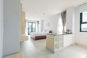Una habitación de hotel moderna con cama, kitchenette, un amplio ventanal y vista a la ciudad.