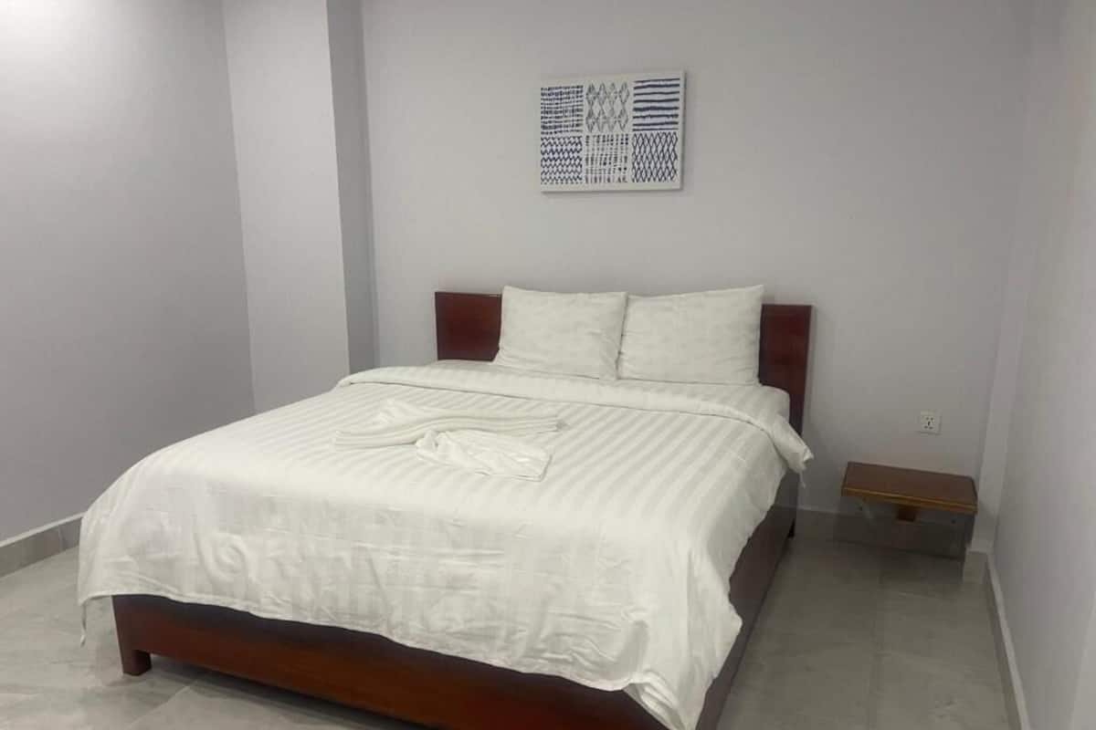A bedroom with a bed, a nightstand, a wall-mounted artwork, and a light switch.