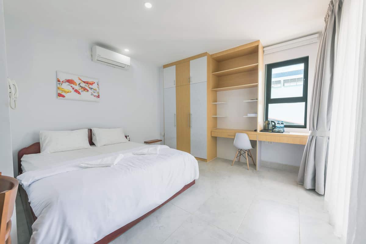 A bedroom with a bed, a desk, a chair, a wardrobe, and a window with curtains.