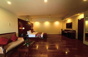 A hotel room with a bed, a sofa, a desk, and a mirror. - Allure Grand Resort (Manali)