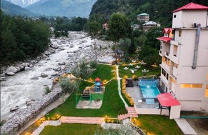 A hotel with a swimming pool, a playground, and a view of a river. - Allure Grand Resort (Manali)