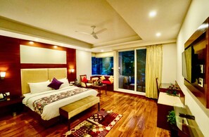 A hotel room with a bed, a desk, a chair, a TV, and a large window. - Allure Grand Resort (Manali)
