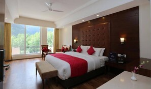A hotel room with a large bed, a desk, a chair, a TV, and a view of greenery. - Allure Grand Resort (Manali)