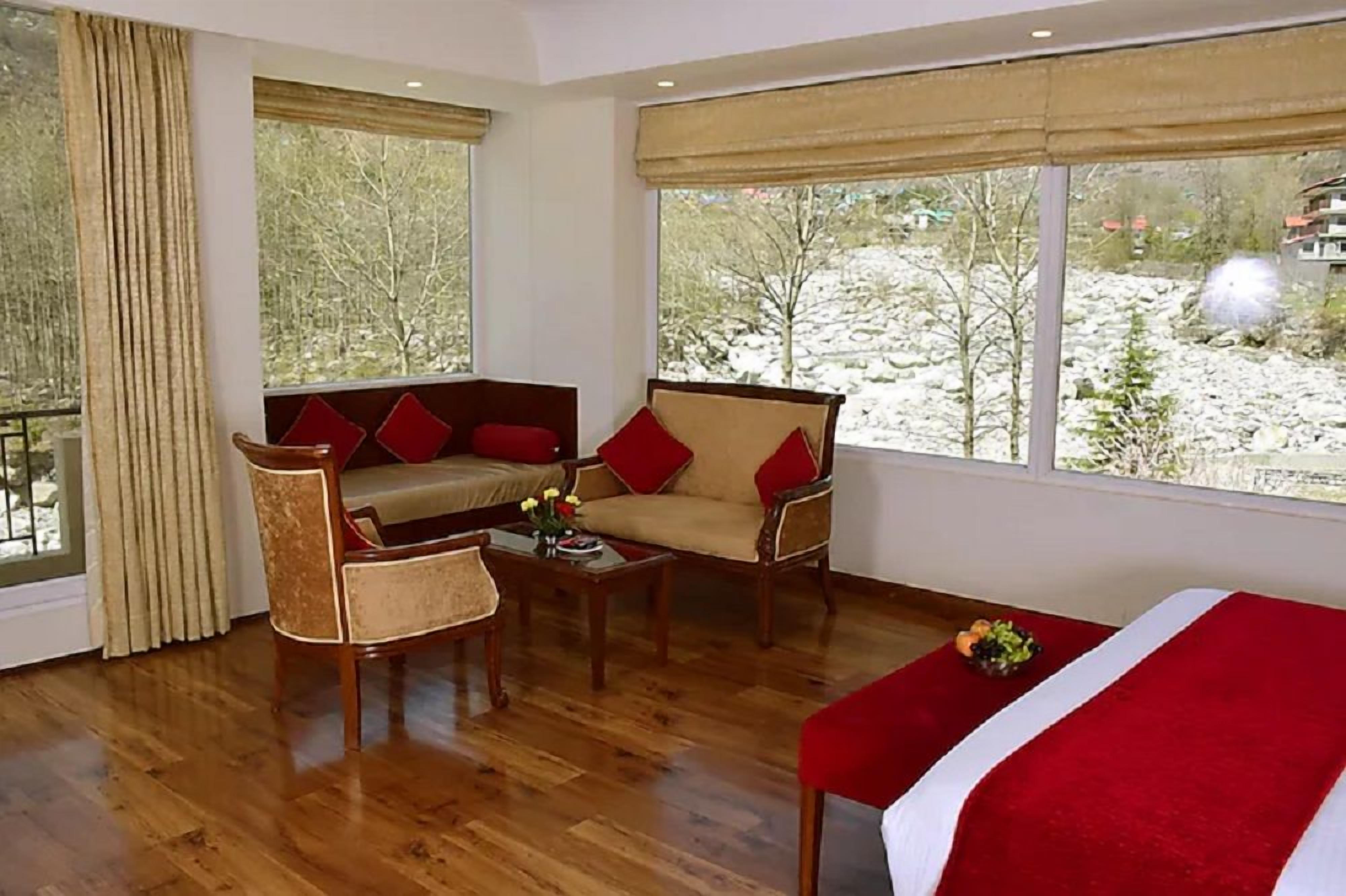 A room with a sofa, armchair, and a bed with a red blanket.
