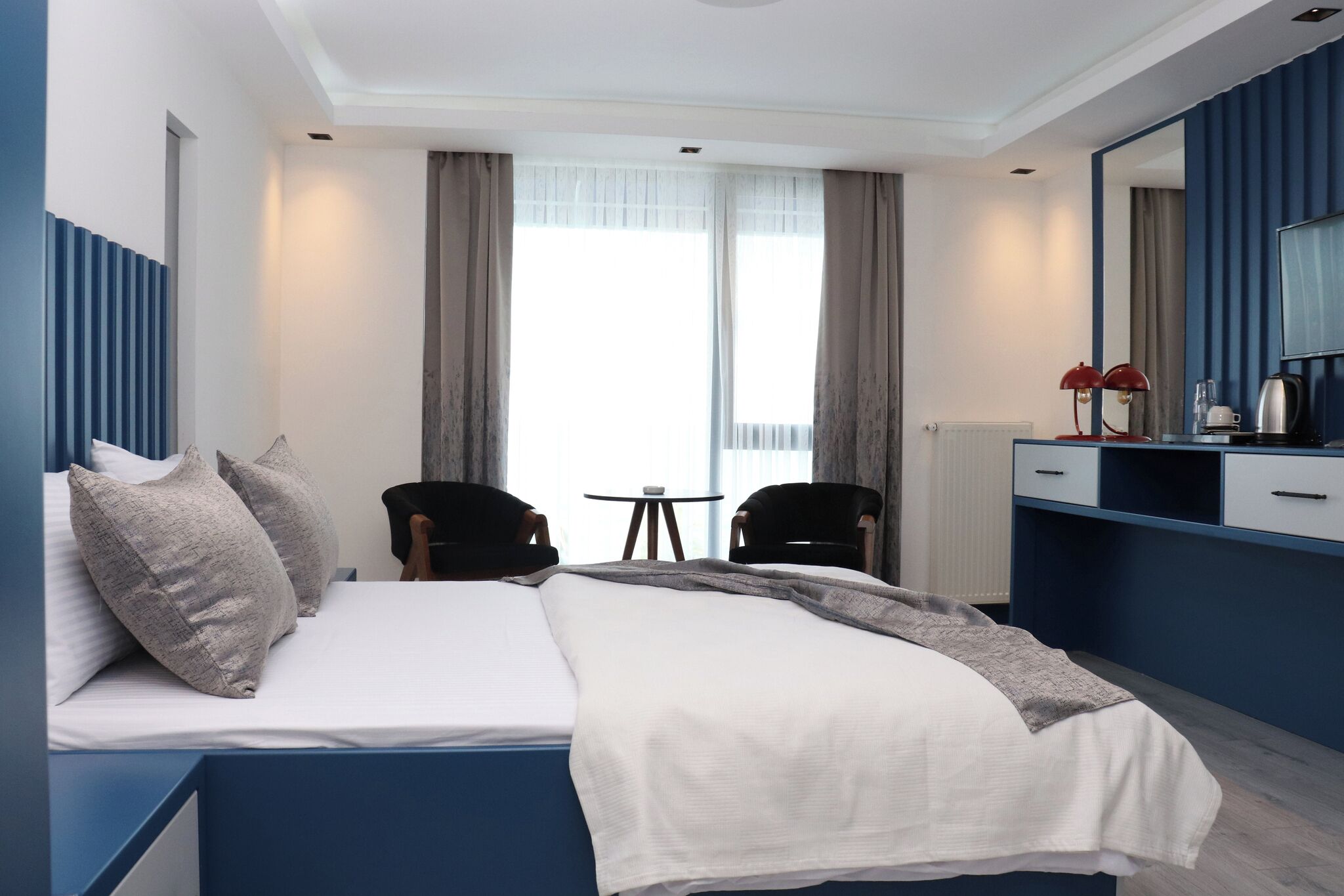 Moderni hotellihuone, jossa on sänky, kaksi tuolia, pieni pöytä, peili ja näkymä ulos.